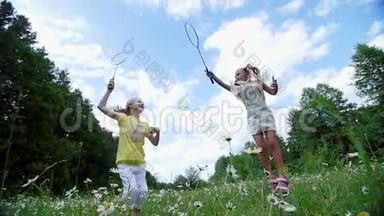 在绿色的洋甘菊草坪上，女孩，<strong>孩子</strong>们，<strong>打羽毛球</strong>，。 他们跑，跳，到处乱跑。 他们玩得很开心。 夏季